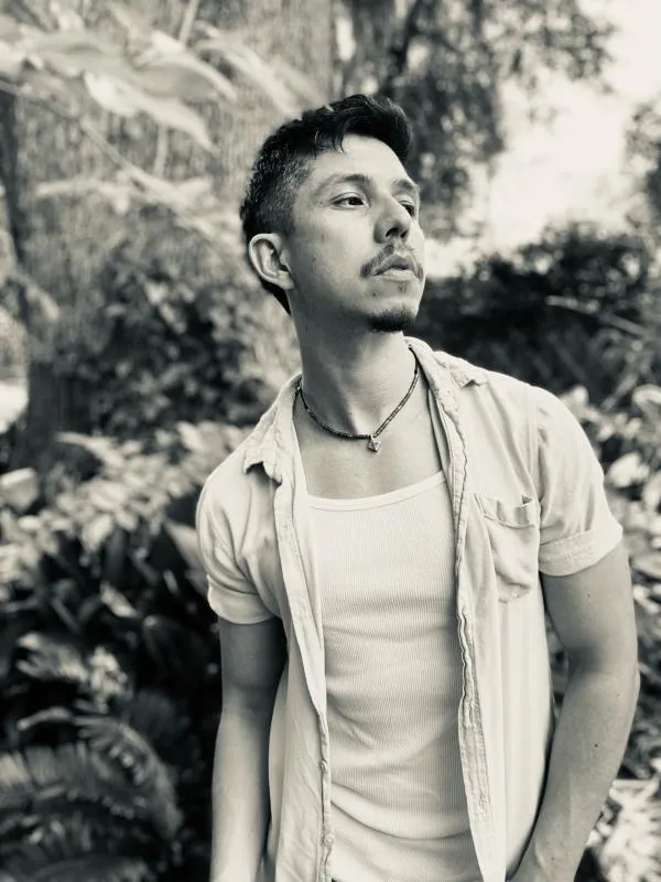 Black and white photo of Irvin Gonzalez wearing a white shirt against a background of trees and foliage.